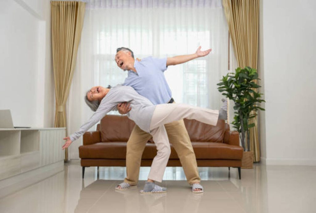 An elderly couple joyfully dancing in their living room.