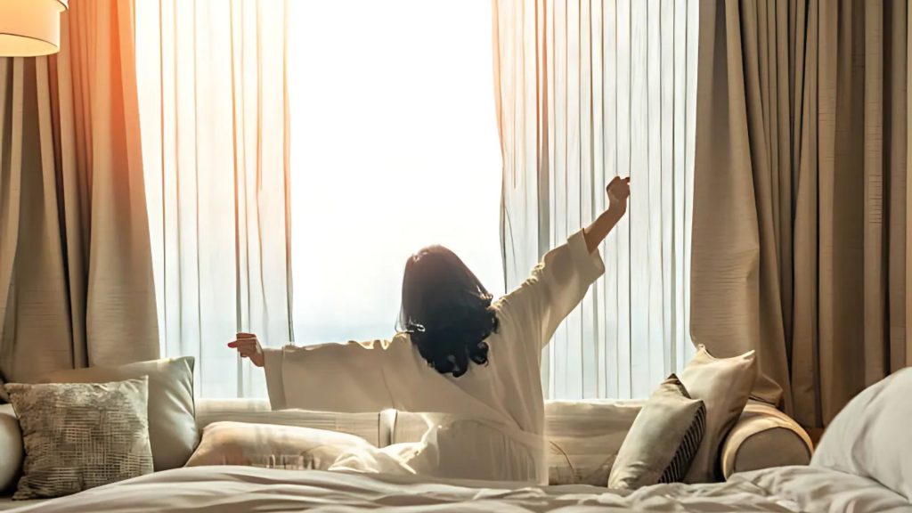 Woman stretching and enjoying the morning sunlight in bed.