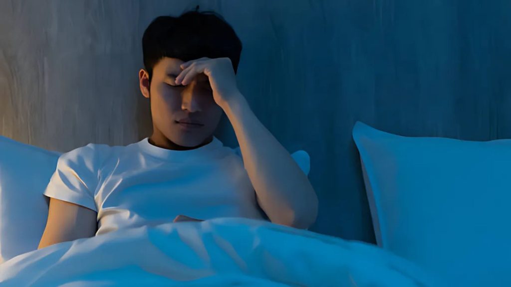Man holding his head in bed, struggling with sleep.